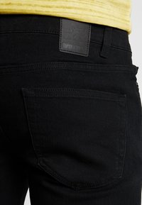 Jeans de mezclilla negra con una textura suave, que presentan un bolsillo trasero y una etiqueta de cuero de la marca en la cintura.