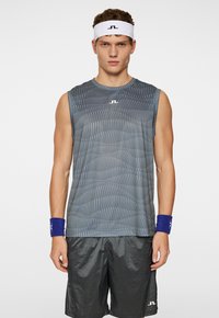 Top atletico grigio senza maniche con un motivo a strisce ondulate, abbinato a pantaloni corti neri lucidi e una fascia bianca con logo. Inclusi polsini blu.