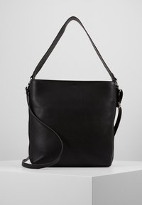 Borsa a spalla nera in pelle con due manici, uno corto per il trasporto a mano e uno lungo e regolabile per l'uso a tracolla, appoggiata su una superficie bianca.