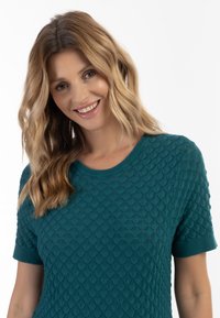 Top tricotat de culoare teal cu mâneci scurte, având un design texturat care asemănă cu solzi, decolteu rotund și un finisaj neted al materialului.