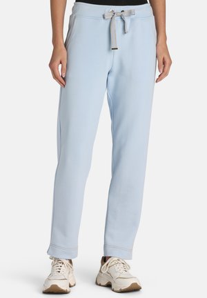 Lyseblå sweatpants med snøre i taljen og sidelommer båret med hvide chunky sneakers på en stående person.