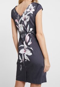 Robe gris foncé avec un dos en forme de V, ornée d'un motif floral en nuances de rose et blanc sur le côté. Tissu lisse, manches courtes.