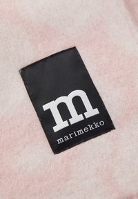 Lyserød filtstof med en rektangulær sort etiket, der har hvid tekst "m" og "marimekko". Teksturen er blød og fuzzy.