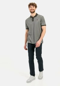 Graues Poloshirt mit dunkelgrünem Kragen und Bündchen, kombiniert mit dunklen Jeans und hellen Turnschuhen. Mit einem Logo auf der linken Brust.