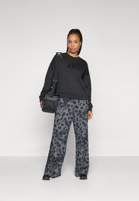Svart sweatshirt med teksturert logo, kombinert med vide grå bukser med svart leopardmønster. Svart crossoverbag og sko.