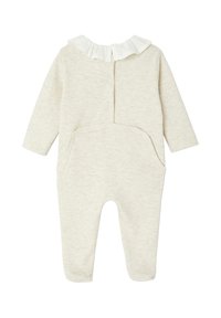 Helles beige Jumpsuit aus weichem Stoff, mit langen Ärmeln, einem Rüschenausschnitt und zwei seitlichen Taschen für zusätzlichen Detail.