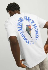 Camiseta de algodón blanca con un gráfico redondo que presenta dos pájaros coloridos y el texto "POLO ALEGRIA SINCE MCMXC" en azul. Manga corta, corte relajado.