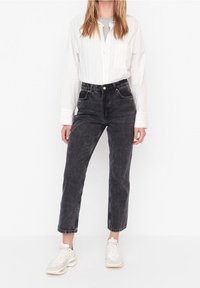 Jean en denim noir taille haute avec une coupe droite, avec des poches avant et une finition délavée, associé à une chemise blanche à rayures.