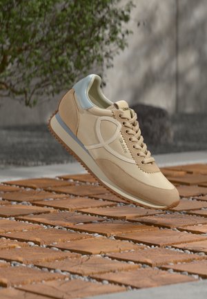 Baskets beige en suède et cuir, avec des accents bleu clair, des lacets plats et une semelle en caoutchouc texturée. Design léger et minimaliste.