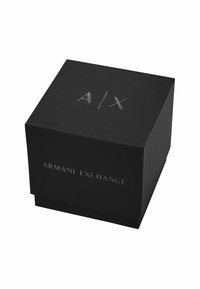 Černá čtvercová krabička s matným povrchem. Na vrchu má vystouplé stříbrné logo "A/X" a na přední straně text "ARMANI EXCHANGE". Čistý design.