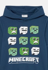 Felpa blu con nove facce di personaggi di Minecraft disposte in una griglia, featuring zombie verdi e scheletri bianchi, con il logo di Minecraft sottostante.