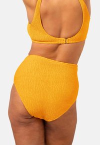 Högmidjade baddräktstassar och matchande bralette i texturerad, ribbad gul väv, med en krokstängning på baksidan och sömlös design.