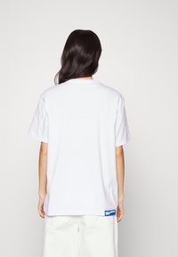 Hvid bomulds t-shirt med afslappet pasform, korte ærmer og rund hals. Har et blåt mærke ved kanten. Glat tekstur.
