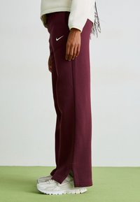 Vinröda sweatpants med en vit Nike-logotyp, med rak bendesign, mjukt material och sidofickor, kombinerat med ljusa sneakers.
