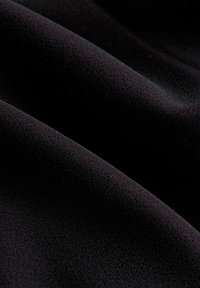 Czarna tkanina o miękkiej, aksamitnej powierzchni. Materiał opada gładko, ukazując delikatne fałdy i bogatą głębię koloru.