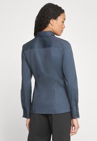 Camicetta navy a maniche lunghe con colletto strutturato, design su misura e polsini con bottoni. Tessuto liscio con un leggero luccichio. Vista posteriore.