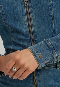 Denimjakke med glidelåslukking, lyseblå vask og kontrasterende søm. Mansjetten har en brodert detalj.