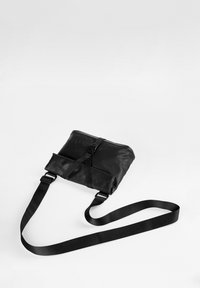 Borsa a tracolla nera in materiale sintetico; dotata di chiusura a pattina, tracolla regolabile e una texture liscia con design minimalista.