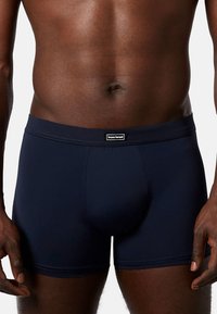 Dark blue fitted boxer shorts made of smooth fabric, featuring a branded elastic waistband and a structured pouch design.