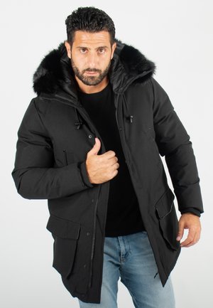 Parka noire avec capuche en fourrure synthétique amovible, fermeture éclair à l'avant et boutons-pression. Dispose de deux grandes poches avant et de poignets côtelés.