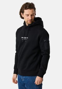 Felpa nera realizzata in morbido tessuto, con tasca a marsupio, cappuccio con cordino regolabile e una toppa sulla manica con unaccento a bottone.