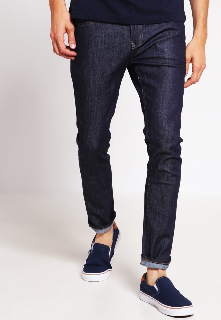 Mörkblå denimjeans med smal passform, med uppvikta fållar och subtila sömnadsdetaljer. Matchas med marinblå slip-on skor.