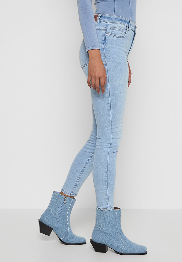 Hellblaue Skinny-Jeans aus Denim mit gestickten Details, kombiniert mit hellblauen Stiefeletten mit quadrater Zehenpartie und stabilen Absätzen.