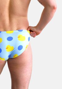 Slip da nuoto blu con stampa di anatroccoli gialli e pois blu. Il tessuto appare liscio ed elastico, con un taglio a vita bassa.