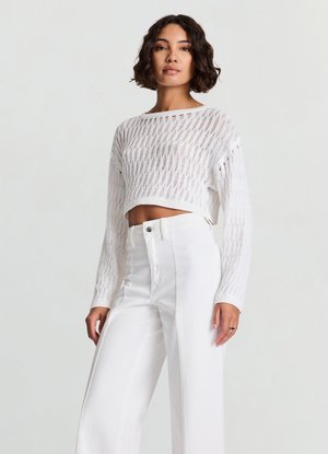 Pull court blanc en maille tricotée avec un motif ajouré, manches longues et encolure ronde, associé à un pantalon blanc taille haute à jambes larges.