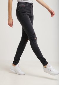 Svarta smala jeans med rivna knän, med femficksdesign och bälteshällor, som kombineras med vita sneakers för en avslappnad look.