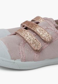 Jasnoróżowy materiałowy but z błyszczącymi różowo-złotymi rzepami, zaokrąglony czubek, biała gumowa podeszwa i gładka tekstura.