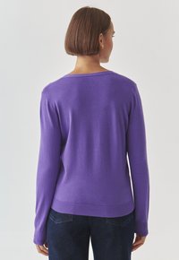 Purple knitted sweater with long sleeves and a rounded neckline. Features ribbed cuffs and hem for added texture and detail.