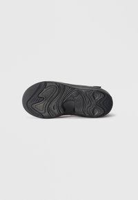 Semelle extérieure de sneaker noire en caoutchouc texturé, avec des motifs ondulés et des rainures pour une meilleure adhérence. Bout rond et structure de talon solide.