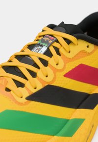 Gros plan d'une chaussure de sport jaune avec des accents orange, vert et noir, des lacets jaunes et une étiquette présentant un visage multicolore.