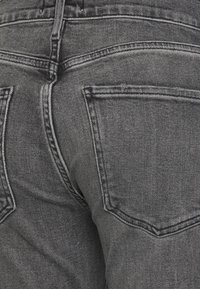 Jeans en denim noir avec une finition texturée, dotés de deux poches arrière et de coutures contrastées le long des coutures.