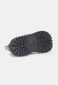 Suela de zapato de goma negra con ribetes profundos y una hendidura circular, que presenta una superficie texturizada y lados reforzados para mayor durabilidad.
