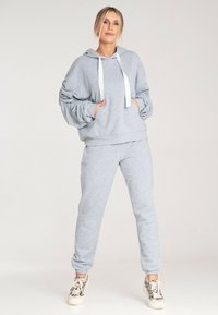 Szara bluza i spodnie w komplecie z miękkiego materiału. Bluza z kapturem posiada kieszeń z przodu, sznurki oraz ściągacze na rękawach. W zestawie z wzorzystymi sneakersami.