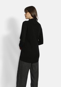 Schwarzer Langarmpullover mit hohem Kragen. Hat eine weiche Textur und eine lockere Passform, die leicht unter die Hüften reicht.