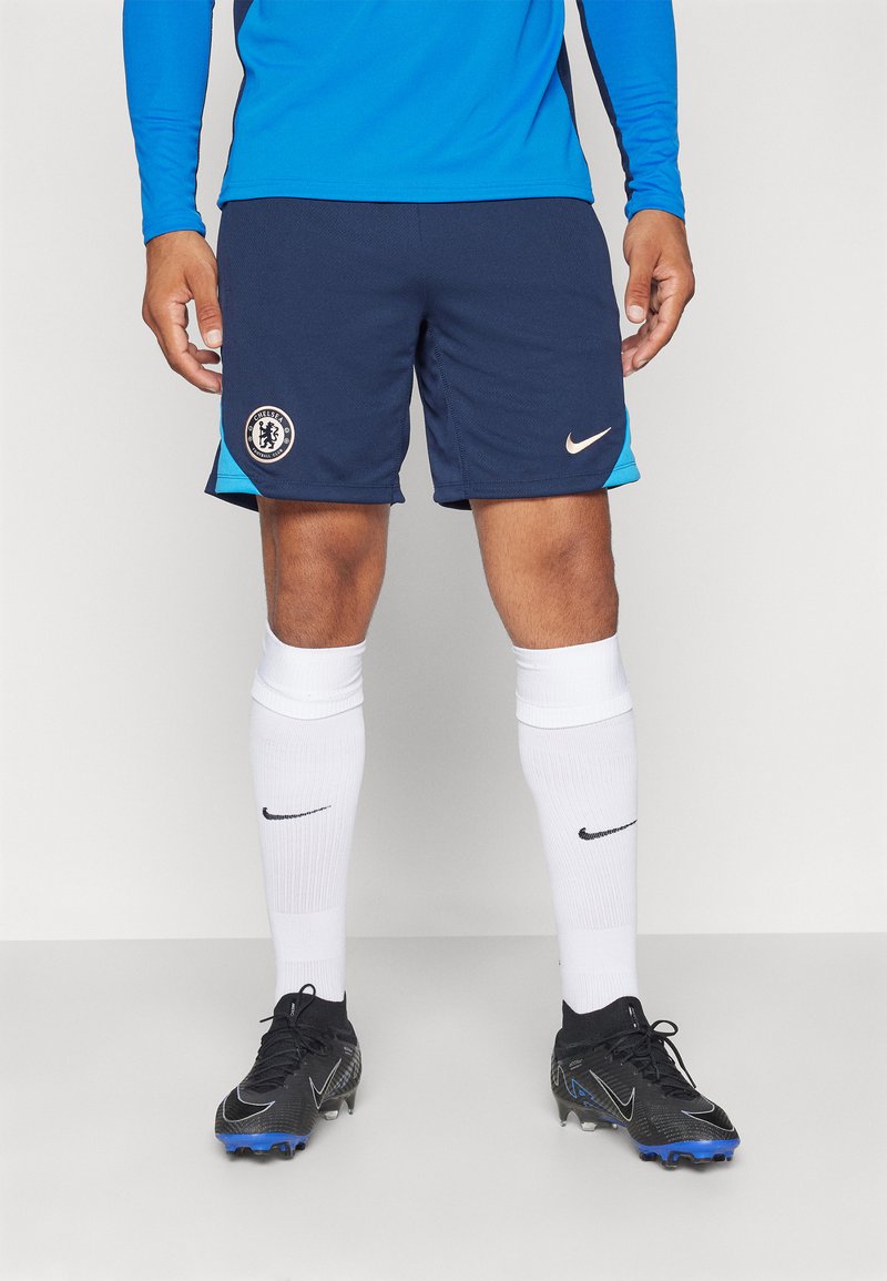 Marineblå fodboldshorts med lyseblå accenter, prydet med Chelsea FC logo, parret med hvide knesokker og sorte Nike fodboldstøvler.