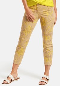 Beige byxur med blommönster och gul broderi, kort design och figurnära silhuett. Kombinerat med vita slip-on-sandaler.