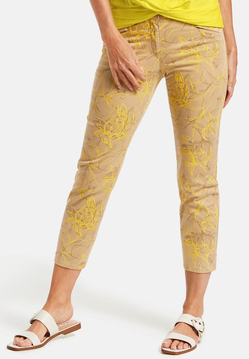 Beige byxur med blommönster och gul broderi, kort design och figurnära silhuett. Kombinerat med vita slip-on-sandaler.