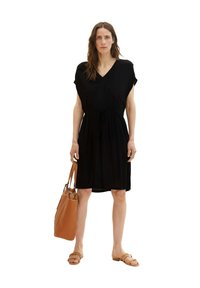 Schwarzes knielanges Kleid mit V-Ausschnitt, kurzen Ärmeln und gerafftem Taillenschnitt, kombiniert mit einer beigen Handtasche und braunen Sandalen. Glatte Stoffstruktur.