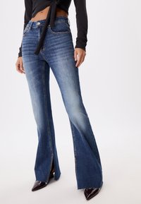 Farkut, jotka ovat leveälahkeiset ja keskisiniset, kevyesti kulutetut yksityiskohdat. Niissä on korkea vyötärö ja vetoketjut lahkeensuissa. Korostettu kuparinvärisillä yksityiskohdilla.