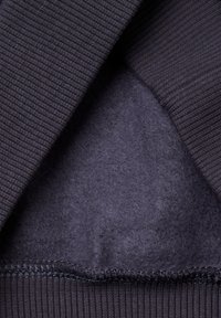 Interior de sudadera gris oscuro con textura acanalada, forro suave y peludo, y dobladillo cosido en contraste.