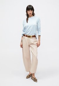 Μακρυμάνικο πουκάμισο με ριγέ σχέδιο σε ανοιχτό γαλάζιο και λευκό, μπεζ παντελόνι με φαρδύ πόδι, καφέ ζώνη με χρυσή αγκράφα και μοκασίνια με λεοπάρ σχέδιο.