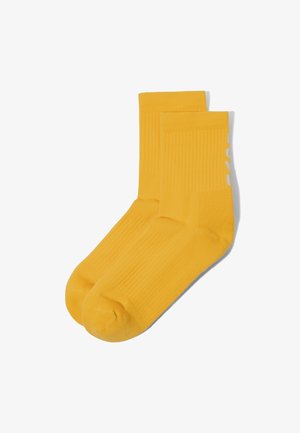 Paar hellgelbe Crew-Socken mit gerippter Struktur, teilweise weißen Text an der Seite zeigend, flach auf weißem Hintergrund liegend.