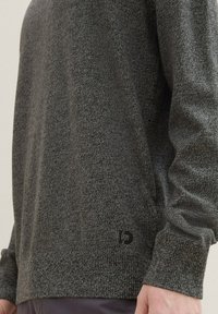 Pull en tricot gris avec un tissu texturé, encolure ronde et manches longues. Petit logo noir en détail sur l'ourlet.