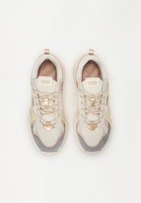 Calçado com parte superior em malha na cor creme, com detalhes em cinza e rosa, acabamentos metálicos e sola de borracha. Rótulo da marca visível na lingueta.