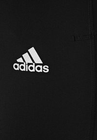 Czarne sportowe szorty wykonane z elastycznego materiału o gładkiej fakturze. Po lewej stronie znajduje się biały logo Adidas.
