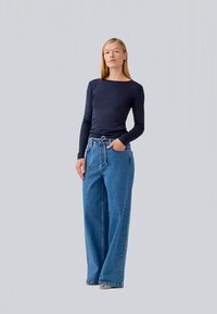 Top de manga longa azul marinho combinado com jeans azuis de cintura alta e corte solto, com um cinto para dar nó. Textura de tecido suave, design casual.
